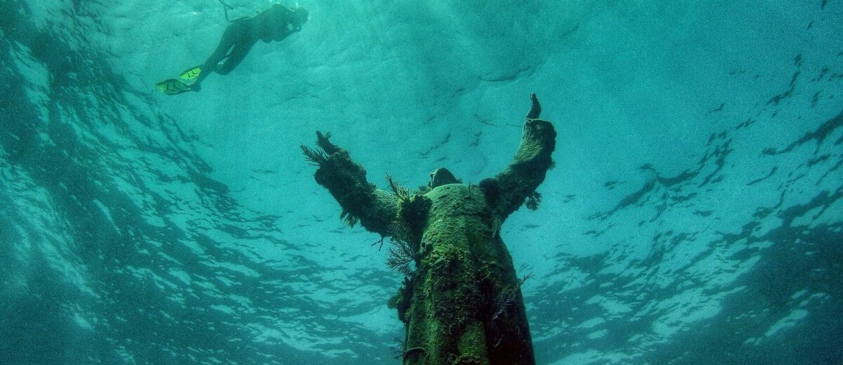 The Christ of the Abyss bronze statue underwater at Key Largo Dry Rocks with a snorkeler swimming above it