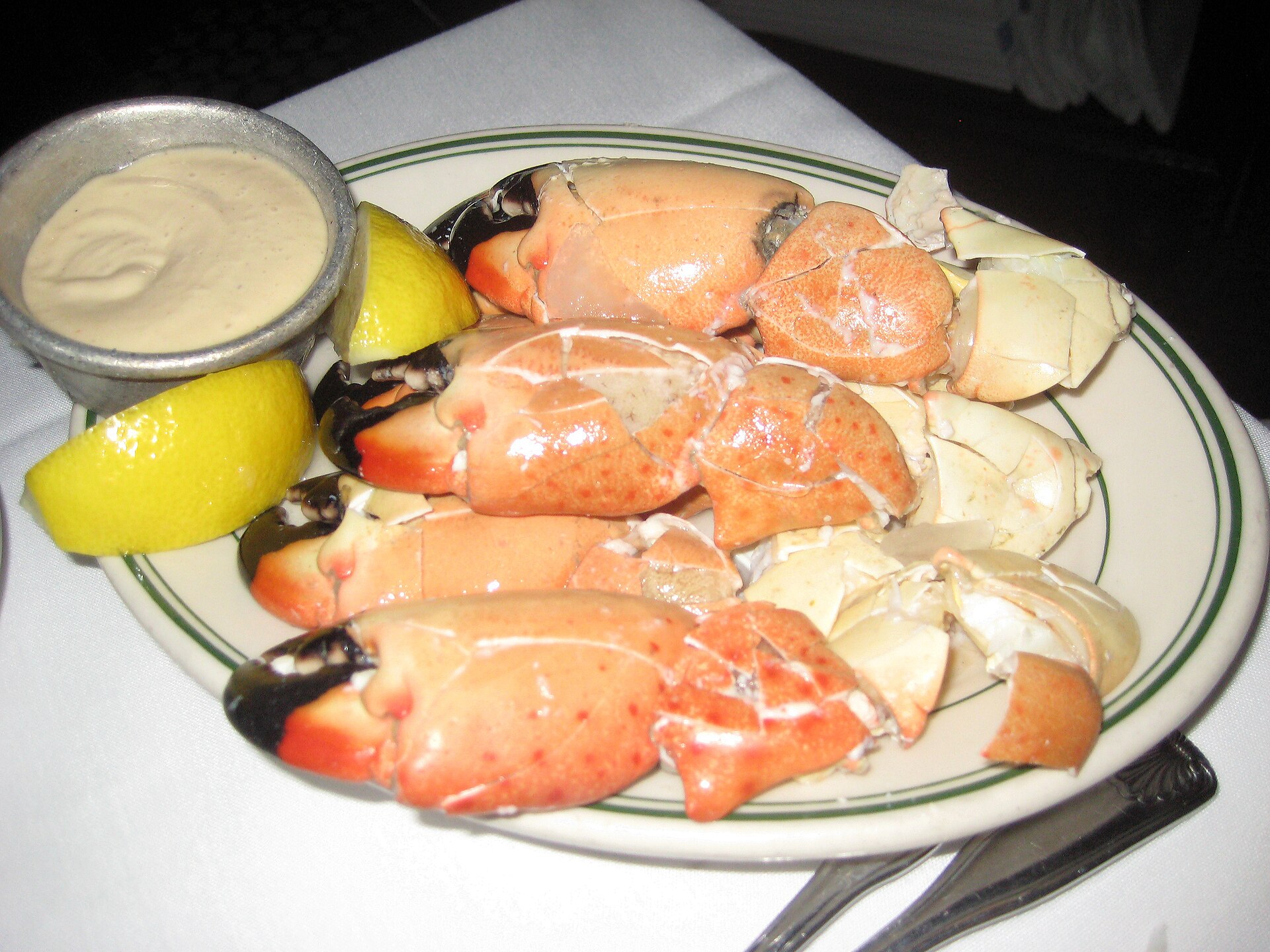 A plate of cracked Florida stone crab claws with lemon wedges and a cup of mustard dipping sauce