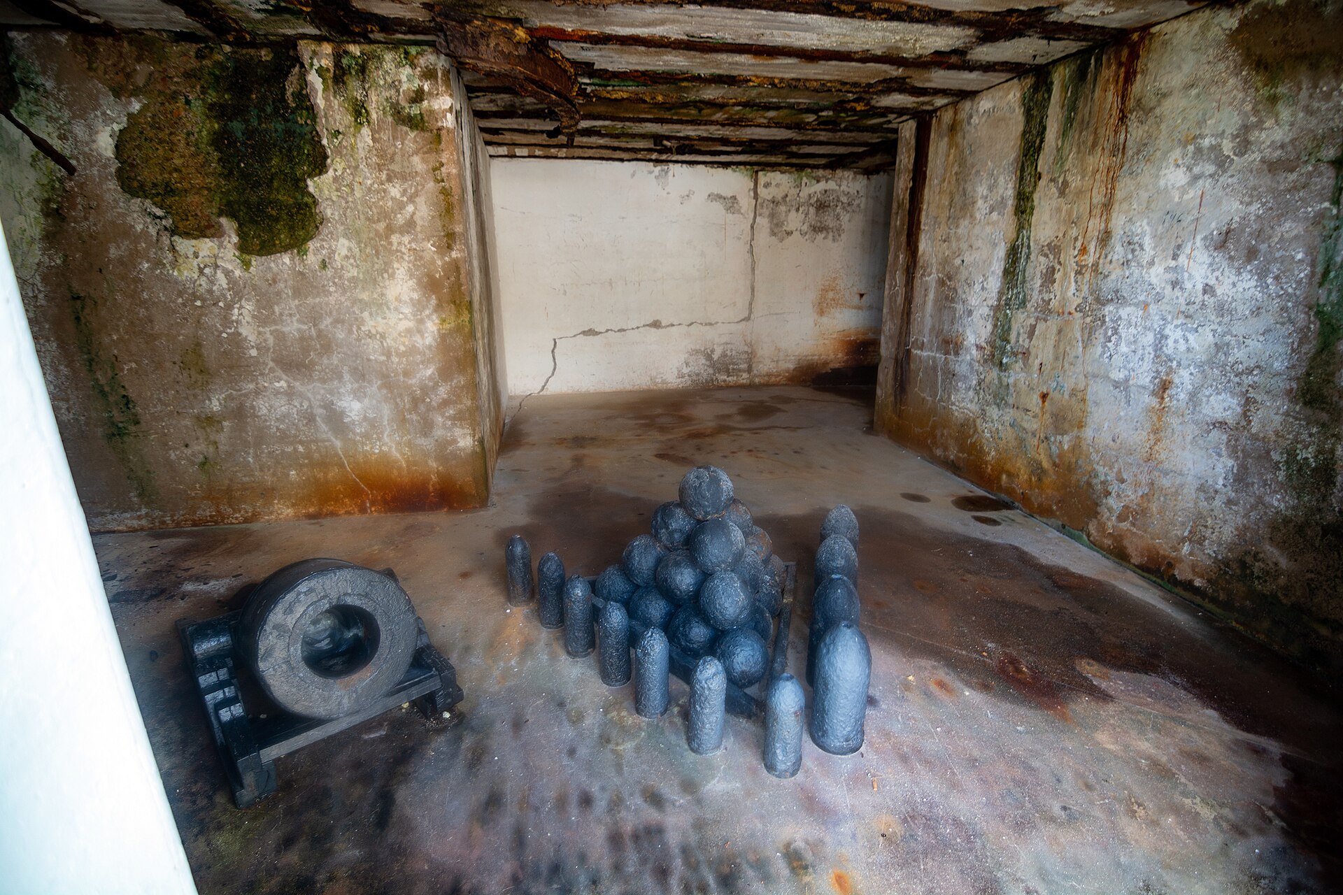 A stack of cannonballs and shells beside an old cannon barrel inside a weathered casemate at Fort Zachary Taylor in Key West