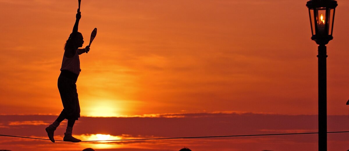 A tightrope walker juggling clubs silhouetted against an orange sunset above the crowd at Mallory Square in Key West