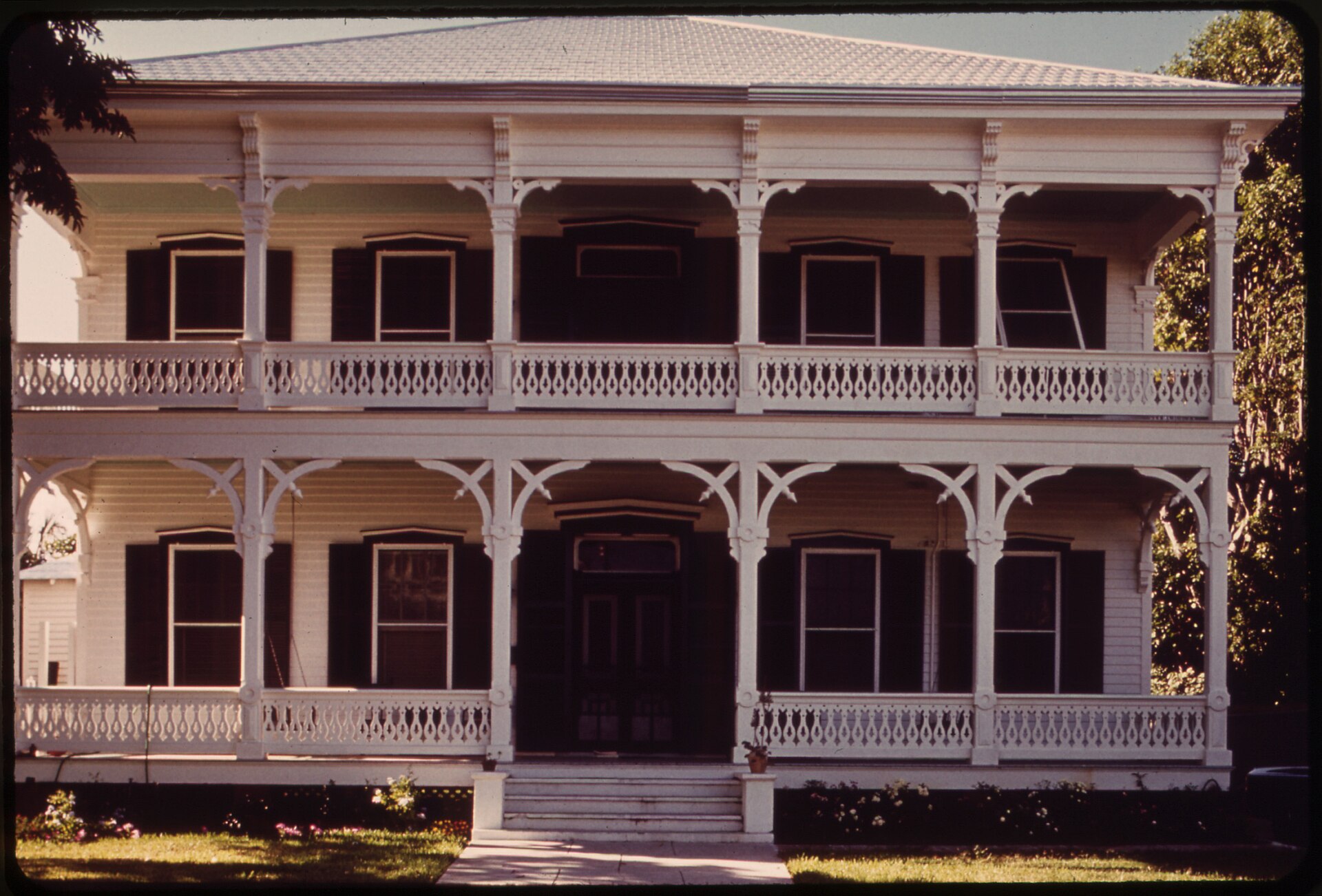 A large two-story white wooden house in Key West with wide double verandas and ornate carved Bahamian-style railings and brackets