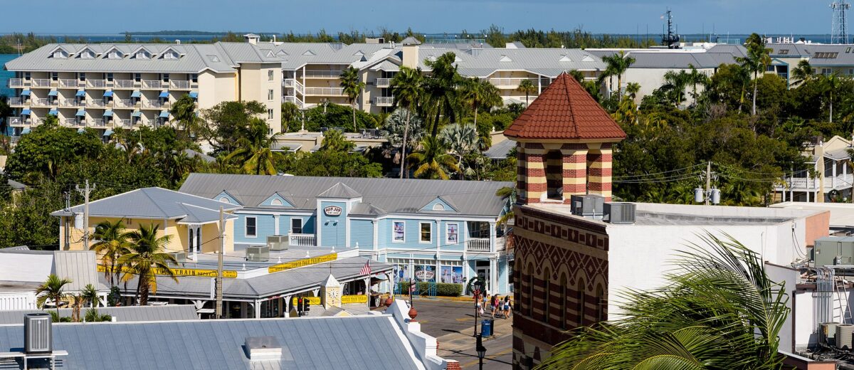 Rooftop view over Old Town Key West at Front and Duval Streets with a striped brick tower, pastel shops, palm trees and the harbor beyond