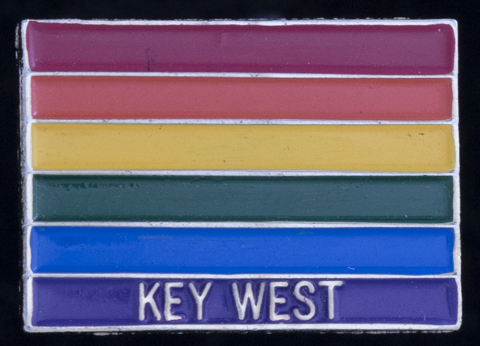 An enamel pin shaped like a rainbow pride flag with the words Key West on the purple stripe
