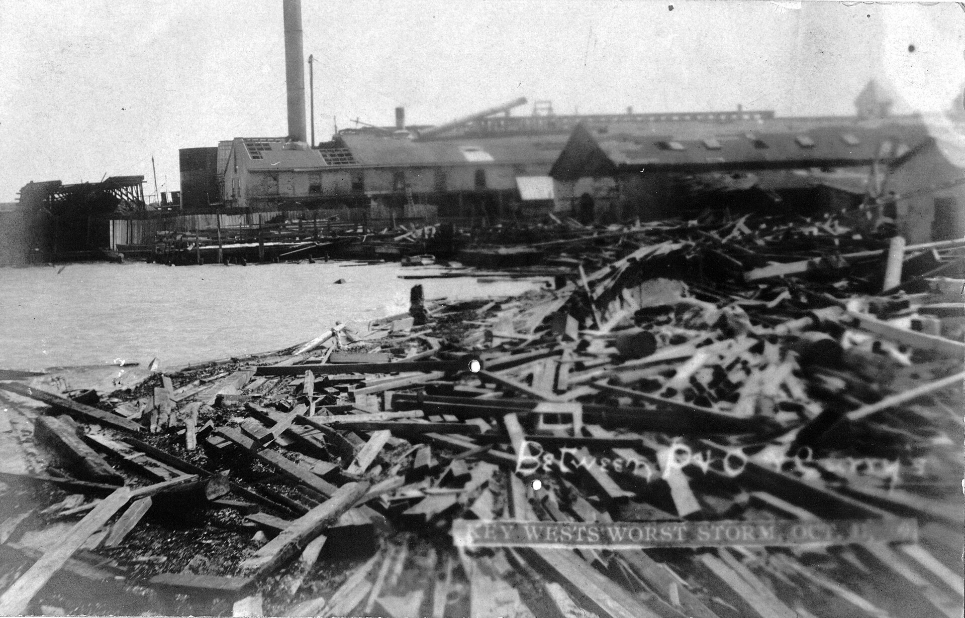 Wreckage of timber and collapsed sheds piled along the Key West waterfront after the October 1909 hurricane, with a factory chimney behind