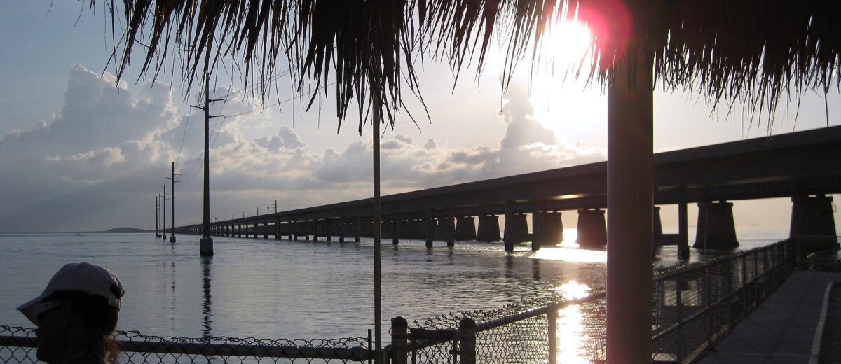 Sunset over the old and new Seven Mile Bridges seen from beneath a thatched shelter at the Marathon end