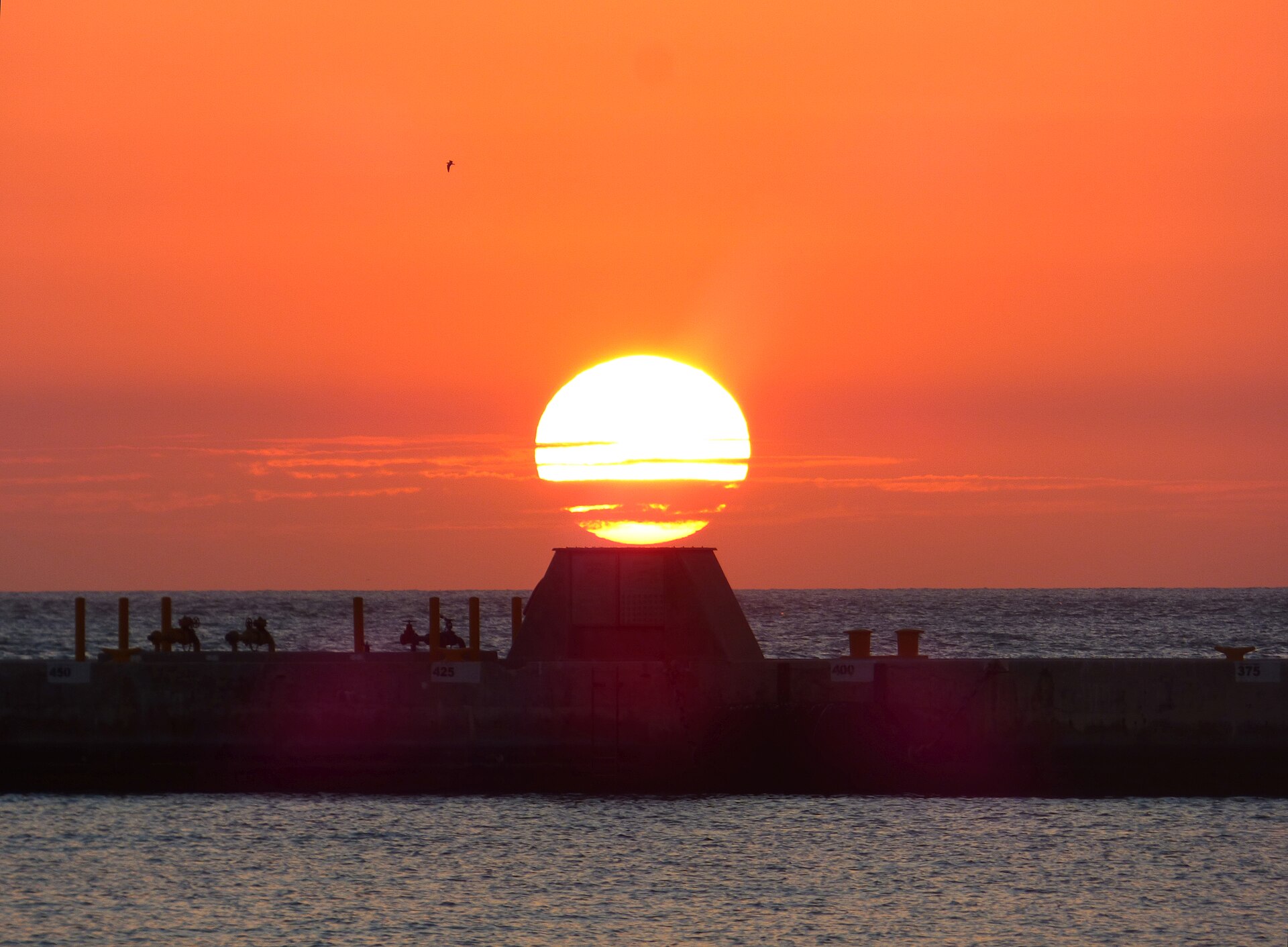 An orange sun setting over the sea behind a concrete pier seen from Truman Waterfront Park in Key West