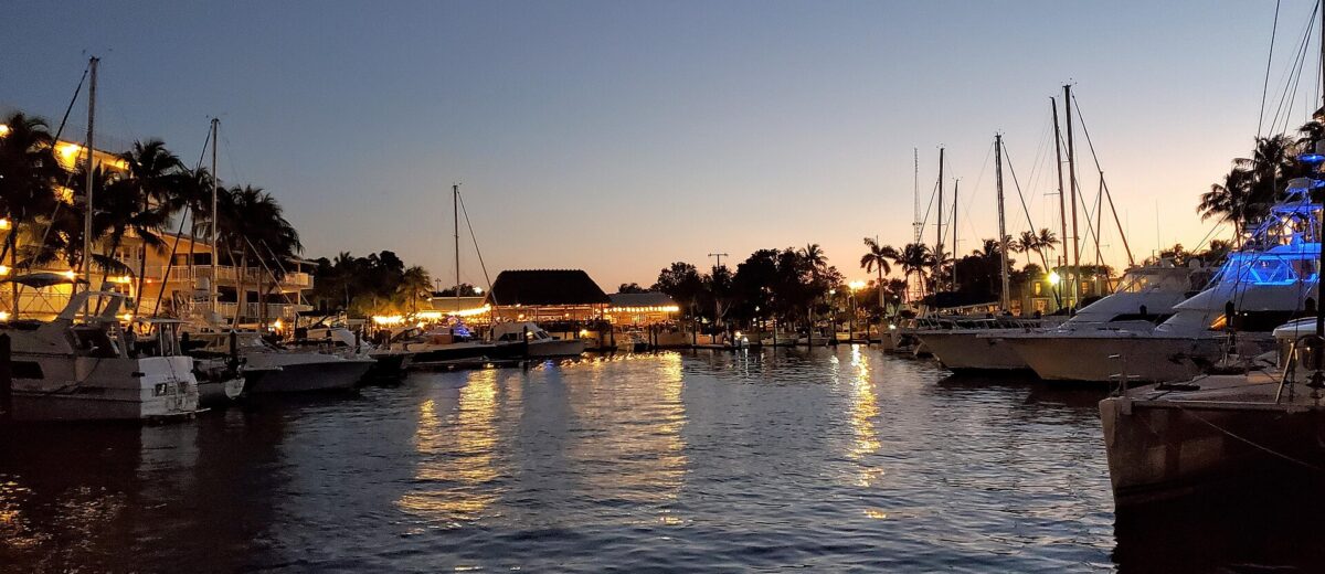 Boats and a lit waterfront hotel and tiki restaurant around a Key Largo marina at dusk