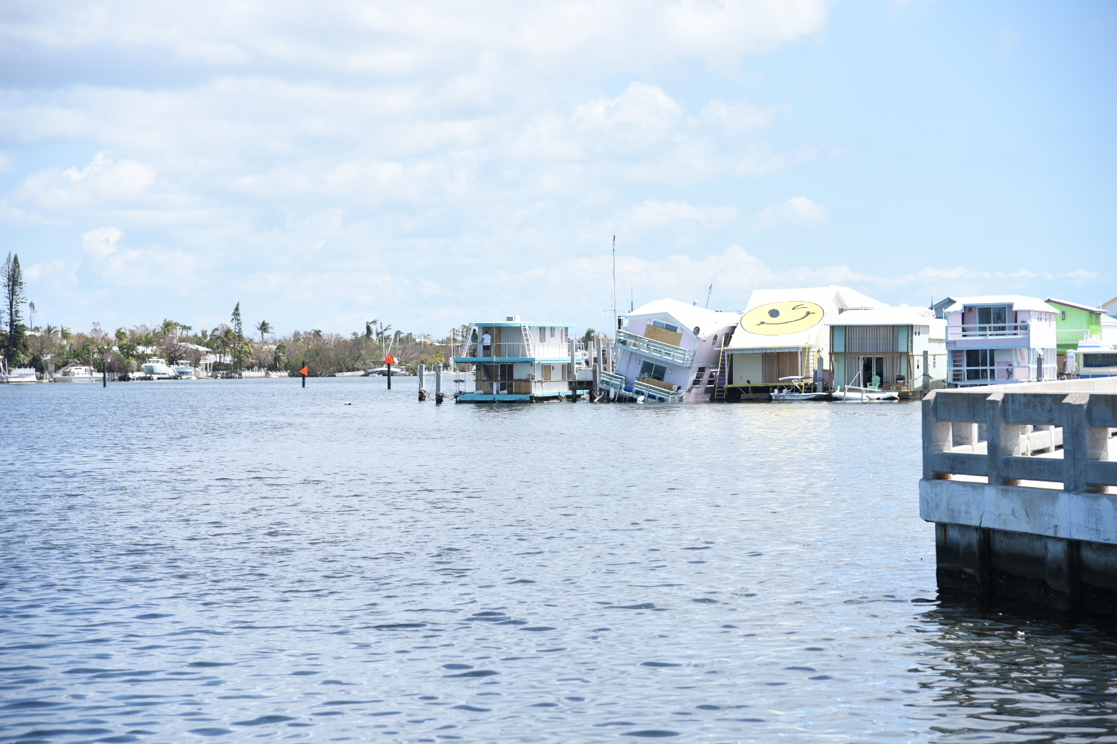 Brightly painted houseboats moored in a row along a waterway, one tilted and half sunk, under a clear sky
