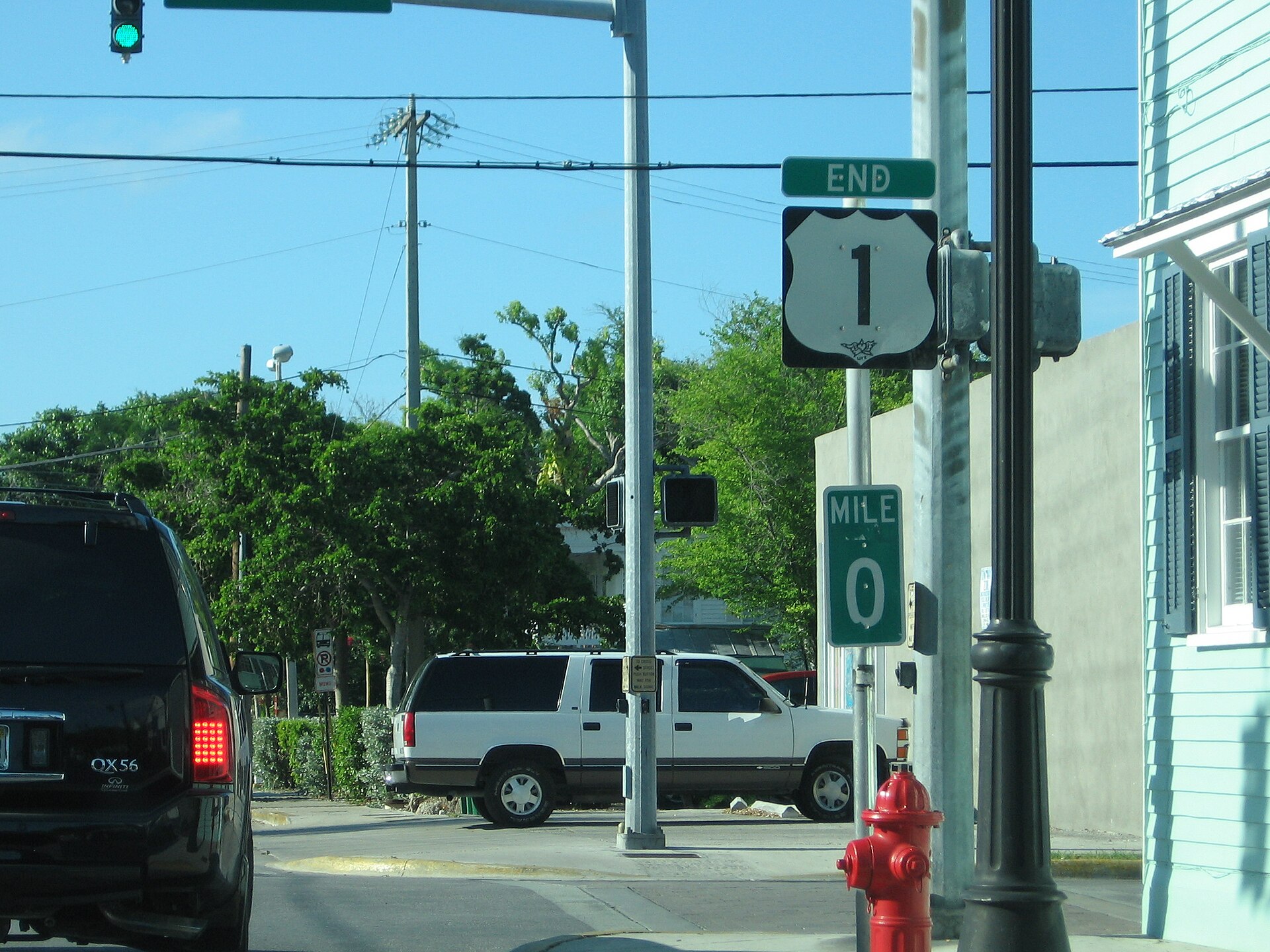Green Mile 0 and End US 1 signs on a pole beside a street with parked cars and a red fire hydrant